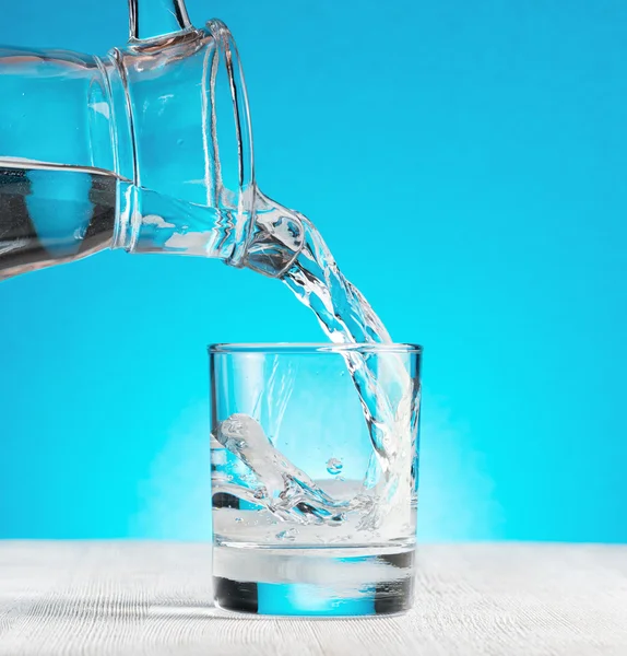 Acqua versando in un bicchiere su sfondo blu — Foto Stock