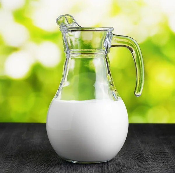 Caraffa di latte su sfondo naturale. Brocca mezza piena — Foto Stock