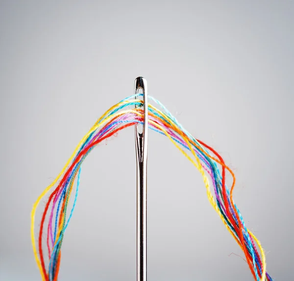 Several colourful threads in a needle — Stock Photo, Image