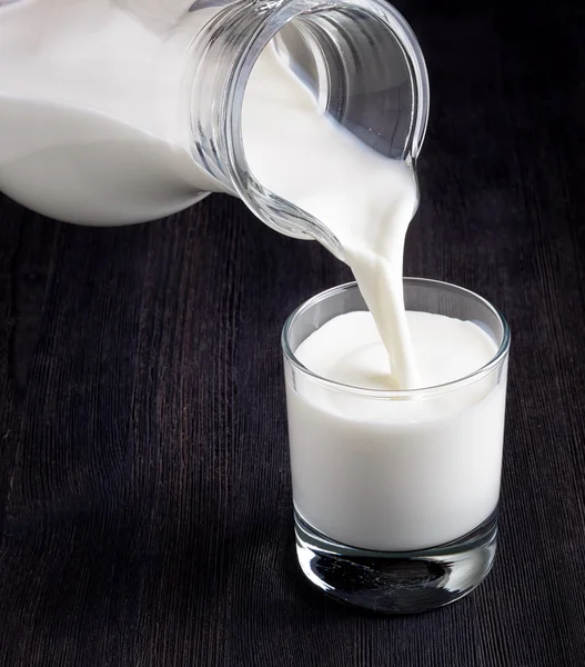 Leche vertiendo en un vaso sobre una pizarra negra —  Fotos de Stock