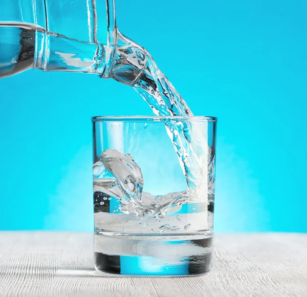 Νερό ρίχνει σε ένα ποτήρι σε μπλε φόντο在蓝色背景上倒进一杯水 — 图库照片