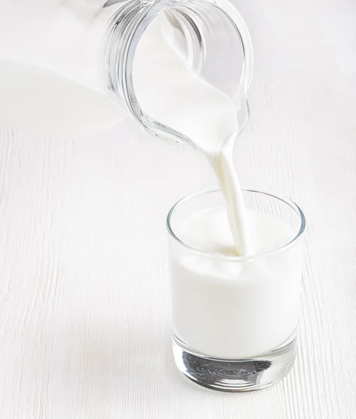 Milk pouring into a glass on white board — Stock Photo, Image