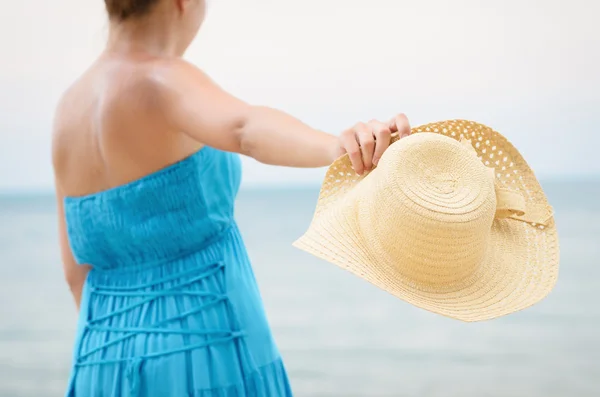 Kobieta w niebieska sukienka wyrzuca kapelusz na plaży — Zdjęcie stockowe