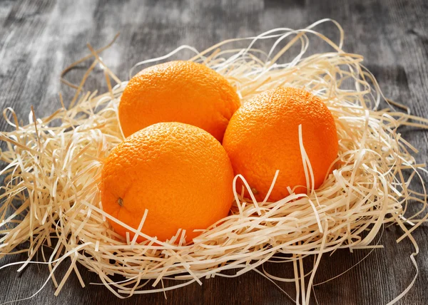 Three oranges in straw on a table. — Stock Photo, Image