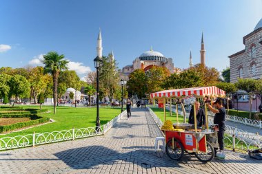 İstanbul, Türkiye - 16 Eylül 2021: Sokak satıcısı Sultanahmet Meydanı 'nda mısır satıyor. Turistler ve halk dinleniyor ve manzaralı şehir parkı boyunca yürüyorlar. Ayasofya 'nın muhteşem manzarası.