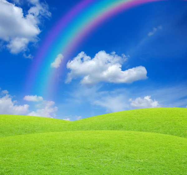 Green field on blue sky with rainbow — Stock Photo, Image