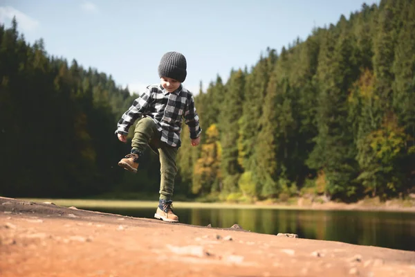 Μικρό παιδί με καρό πουκάμισο και γκρι καπέλο στην ακτή της λίμνης του δάσους — Φωτογραφία Αρχείου