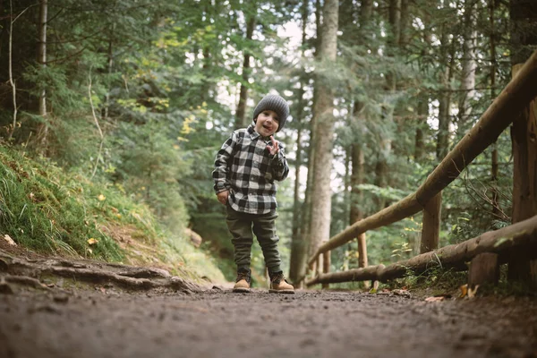 Small kid in a plaid shirt and gray hat in the forest — Stock Photo, Image