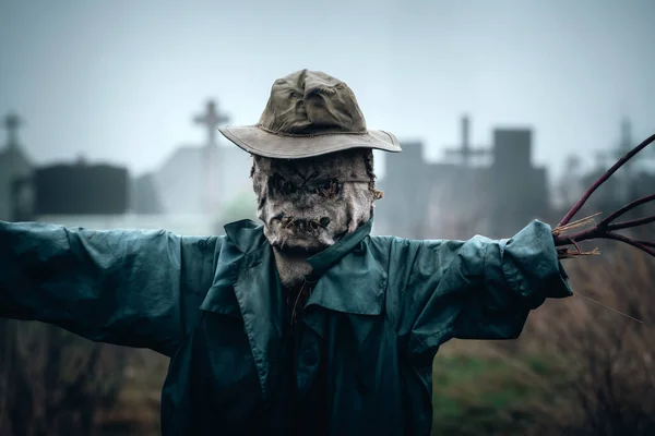Terribile spaventapasseri in mantello scuro e cappello sporco si erge da solo su un cimitero — Foto Stock