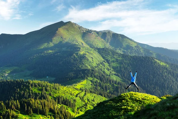 Un turista en el borde de una montaña cubierta con una hierba exuberante — Foto de Stock