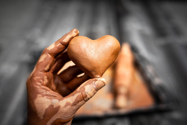 Heart made of potters clay in the hands of a master potter. Love concept
