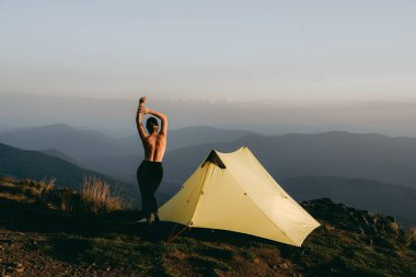 Alone girl near yellow tent against the backdrop of an incredible autumn mountains landscape