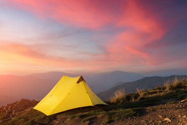 Yellow tent against the backdrop of an incredible mountain landscape during gorgeous sunset. Amazing highland. Tourism concept