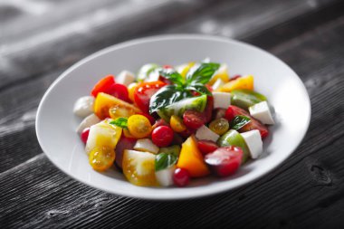 Salad with different varieties kind of red, yellow, green and black tomato mix, mozzarella cheese and basil. Caprese salas with fresh colourful tomatoes. Food photography