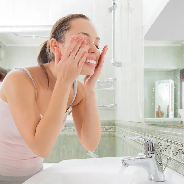 Mujer joven lavándose la cara con agua limpia — Foto de Stock