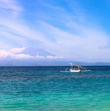Agung Dağı aktif yanardağ Nusa Penida, Bali Adası, Endonezya 'da bulutlarla kaplı. Beyaz kumsalda jukung adında geleneksel balıkçı tekneleri. Köpüklü dalgalar kıyıya yayıldı..