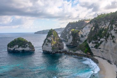 Kumsal, turkuaz okyanus ve dağlarla güneşli bir gün manzarası. Diamond Sahili, Nusa Penida, Bali Adası, Endonezya. Duvar kağıdı arka planı. Doğal bir manzara. Romantik rahatlama yeri. Dalgalar.