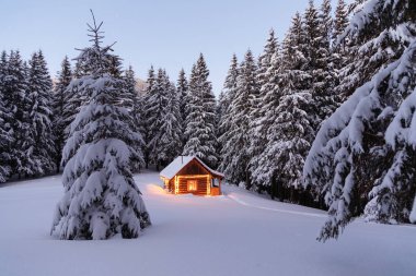 Lambalar akşam vakti evi aydınlatıyor. Kış manzarası. Çimenlikteki ahşap kulübe karla kaplı. Gizemli bir gece. Noel 'i ve yeni yılı kutlarım. Dağlar ve ormanlar. Duvar kağıdı arkaplanı.