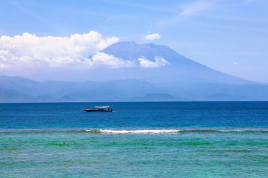 Agung Dağı aktif yanardağ Nusa Penida, Bali Adası, Endonezya 'da bulutlarla kaplı. Beyaz kumsalda jukung adında geleneksel balıkçı tekneleri. Köpüklü dalgalar kıyıya yayıldı..