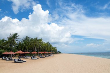 Şemsiyeli ve şezlonglu boş plaj. Palmiye ağaçları. Güzel yaz manzaralı deniz manzarası. Endonezya 'nın Bali adalarında rahatla.