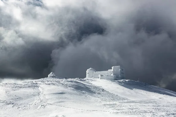 Winter scenery. A panoramic view of the old observatory covered with textured snow. Beautiful landscape of high mountains, foggy sky. Lawn covered with white snow. Wallpaper snowy background.