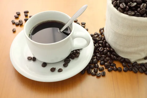 Taza de café y granos de bolsa en la mesa de madera —  Fotos de Stock