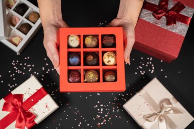 Kırmızı bir kutuda, kadınların elinde, arka planda bulunan çeşitli el yapımı çikolatalı trüf şekerleri..