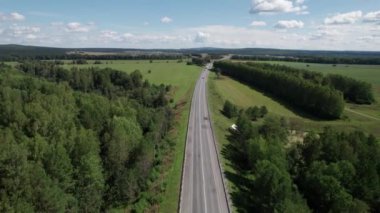 Güneşli bir yaz sabahında çam ağaçlarıyla yeşil ağaçlar arasındaki hava manzaralı yol. Sibirya, Rusya 'da doğa manzarası. Kozalaklı bir ormandan geçen bir yol, İHA 'dan havadan çekilen bir görüntü..