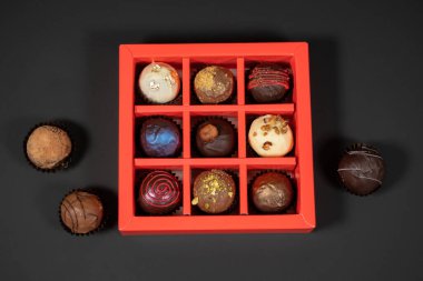 Koyu arkaplanda kırmızı bir kutuda çeşitli el yapımı çikolatalı şekerler. Üst görünümün tam üstünde.