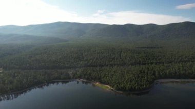 Baykal Gölü 'nün destansı sinematik manzarası. Bir dağ ormanı gölünde çam ağaçlarıyla birlikte turkuaz su. Mavi göl ve yeşil ormanların havadan görünüşü. Dağ ormanları arasındaki göle bak..