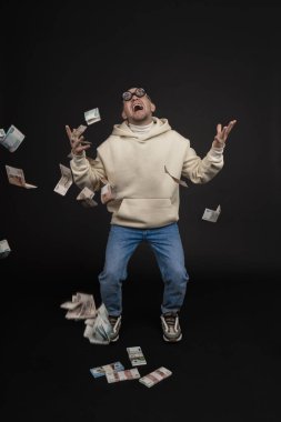 Genç mutlu iş adamı siyah arka planda izole edilmiş bir yığın parayla dans ediyor..