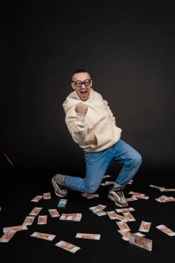 Genç mutlu iş adamı siyah arka planda izole edilmiş bir yığın parayla dans ediyor..