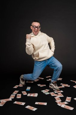 Genç mutlu iş adamı siyah arka planda izole edilmiş bir yığın parayla dans ediyor..