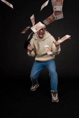 Genç mutlu iş adamı, siyah arka planda izole edilmiş bir yığın para rublesiyle dans ediyor. Nakit para tabancası. Seçici odak, ana konu - erkek.