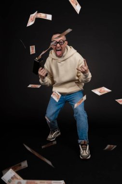 Genç mutlu iş adamı, siyah arka planda izole edilmiş bir yığın para rublesiyle dans ediyor. Nakit para tabancası. Seçici odak, ana konu - erkek.