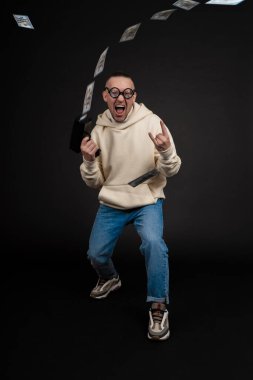 Genç mutlu iş adamı, siyah arka planda izole edilmiş bir yığın para rublesiyle dans ediyor. Nakit para tabancası. Seçici odak, ana konu - erkek.