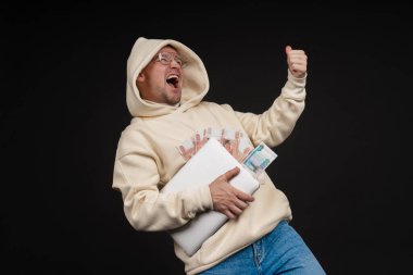 Defteri ve kara arka planda izole edilmiş bir yığın parası olan genç ve mutlu bir iş adamı. Seçici odaklanma, ana konu - adam. İlginç bir iş konsepti.