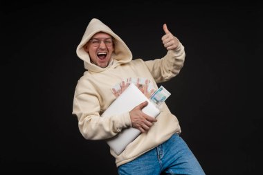 Defteri ve kara arka planda izole edilmiş bir yığın parası olan genç ve mutlu bir iş adamı. Seçici odaklanma, ana konu - adam. İlginç bir iş konsepti.