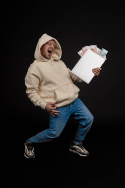 Defteri ve kara arka planda izole edilmiş bir yığın parası olan genç ve mutlu bir iş adamı. Seçici odaklanma, ana konu - adam. İlginç bir iş konsepti.