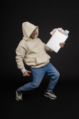 Defteri ve kara arka planda izole edilmiş bir yığın parası olan genç ve mutlu bir iş adamı. Seçici odaklanma, ana konu - adam. İlginç bir iş konsepti.