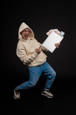 Defteri ve kara arka planda izole edilmiş bir yığın parası olan genç ve mutlu bir iş adamı. Seçici odaklanma, ana konu - adam. İlginç bir iş konsepti.