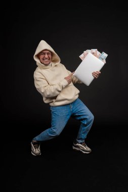 Defteri ve kara arka planda izole edilmiş bir yığın parası olan genç ve mutlu bir iş adamı. Seçici odaklanma, ana konu - adam. İlginç bir iş konsepti.