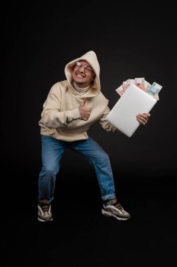 Defteri ve kara arka planda izole edilmiş bir yığın parası olan genç ve mutlu bir iş adamı. Seçici odaklanma, ana konu - adam. İlginç bir iş konsepti.