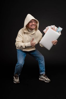 Defteri ve kara arka planda izole edilmiş bir yığın parası olan genç ve mutlu bir iş adamı. Seçici odaklanma, ana konu - adam. İlginç bir iş konsepti.