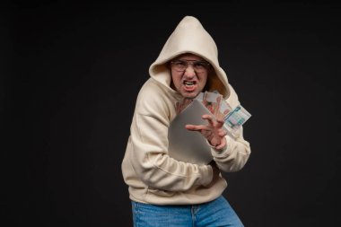 Defteri ve kara arka planda izole edilmiş bir yığın parası olan genç ve mutlu bir iş adamı. Seçici odaklanma, ana konu - adam. İlginç bir iş konsepti.