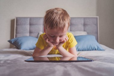 Distance education, learning. Boy is lying on the bed with a tablet in the room. Child with a gadget. Teenage child using tablet pc.