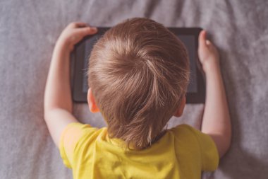Uzaktan eğitim, öğrenme. Oğlan odada bir tabletle yatakta oturuyor. Elinde alet olan bir çocuk. Tablet pc kullanan ergen çocuk.