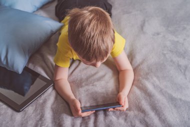 Distance education, learning. Boy is lying on the bed with a smartphone in the room. Child with a gadget. Teenage child using smartphone.