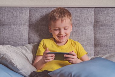 Distance education, learning. Boy is lying on the bed with a smartphone in the room. Child with a gadget. Teenage child using smartphone.