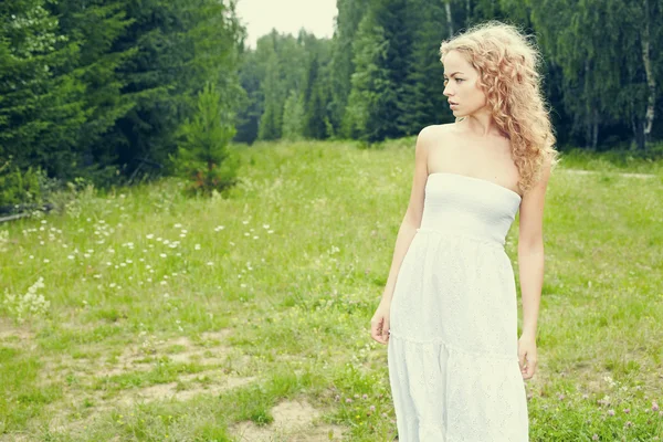 Menina loira bonita no campo verde com flores. Cena rural — Fotografia de Stock